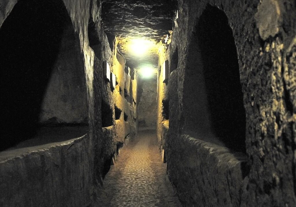 Narrow underground gallery lined with burial niches in the Catacombs of Domitilla, Rome